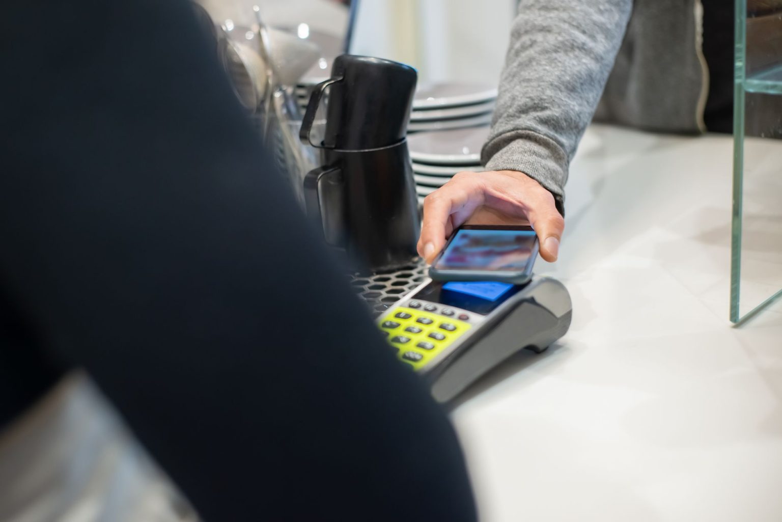Pessoa realiza um pagamento por aproximação com smartphone em um café, usando um terminal eletrônico.