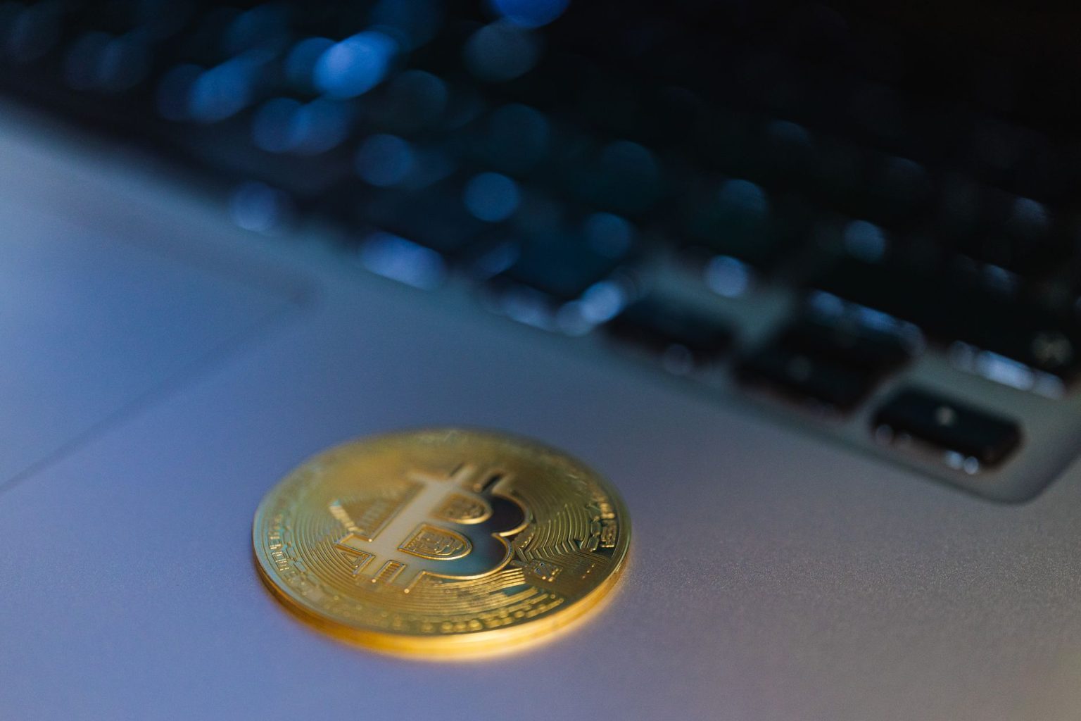 Moeda de Bitcoin em close sobre um laptop, representando a relação entre criptomoedas e tecnologia digital.