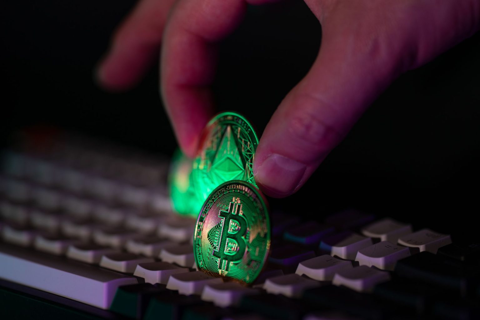 Mão colocando moedas de bitcoin e Ethereum sobre um teclado de computador.