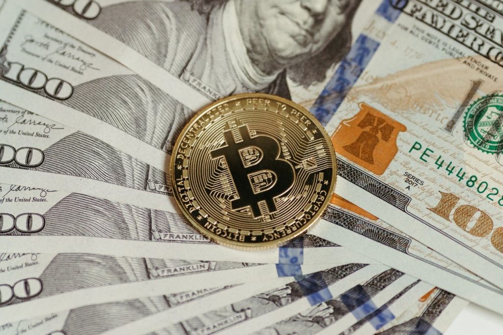 Metaplanet planeja levar 2.100 bitcoins para nova estrutura corporativa nos EUA Moeda de Bitcoin sobre uma pilha de notas de cem dólares.