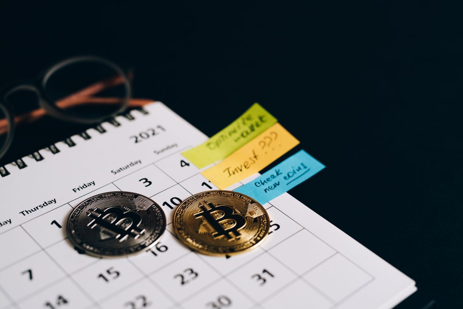Moedas de Bitcoin sobre um calendário com anotações adesivas, representando planejamento de investimentos.